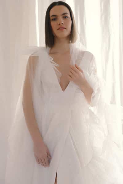 Frau in schlichtem, hochgeschlossenem Brautkleid aus fließendem Crepe Stoff mit Brautstrauß