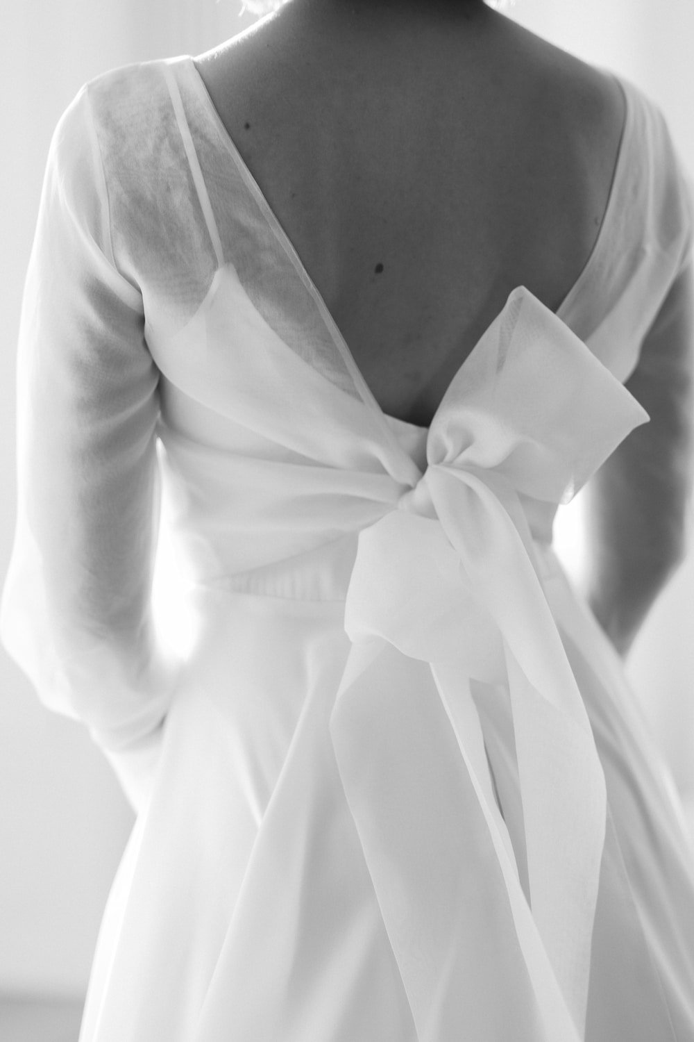 Frau in hochgeschlossenem Brautkleid aus fließendem Crepe Stoff mit Taillenband mit Schleife