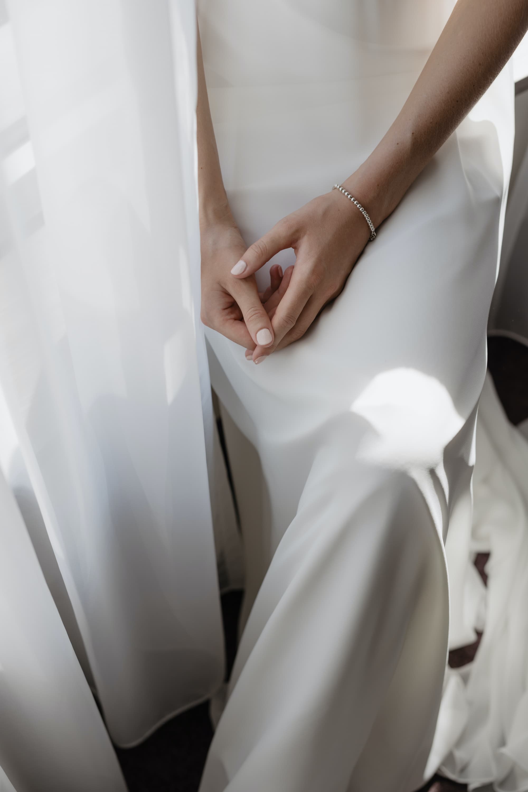 Frau in weißem Brautkleid mit Händen im Schoß
