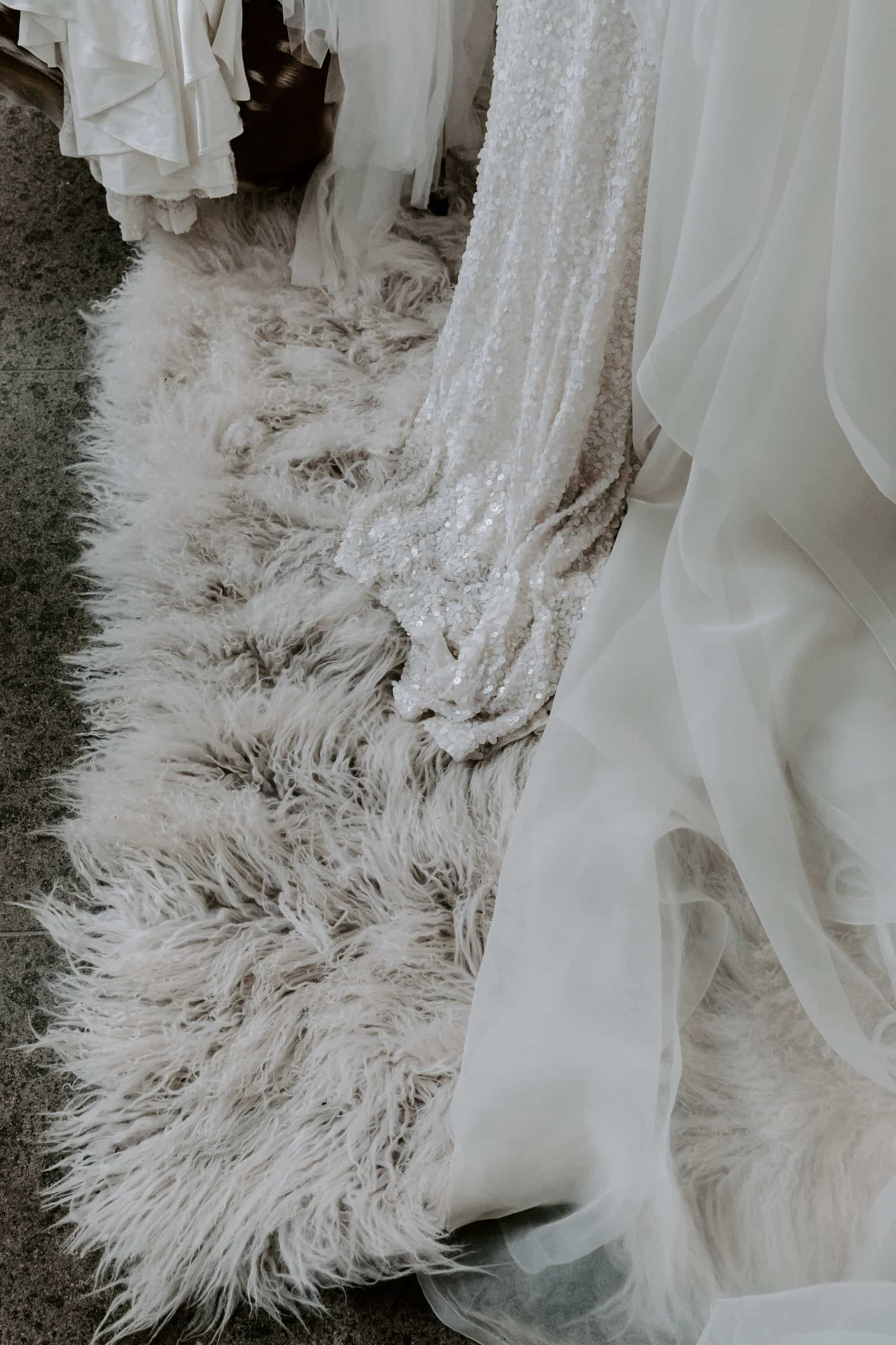 Säume von hängenden Brautkleidern aus Spitze, Satin und Glitzer auf fake fur Teppich